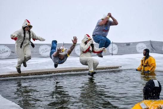 Costumed jumpers mid-air at the Polar Fest Polar Plunge in Detroit Lakes